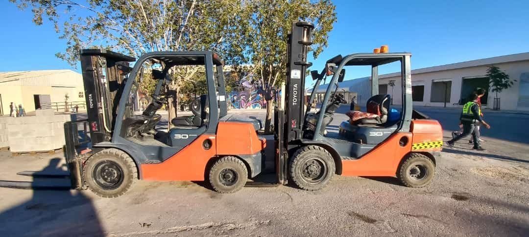 Two forklifts parked side by side on a tree-lined street