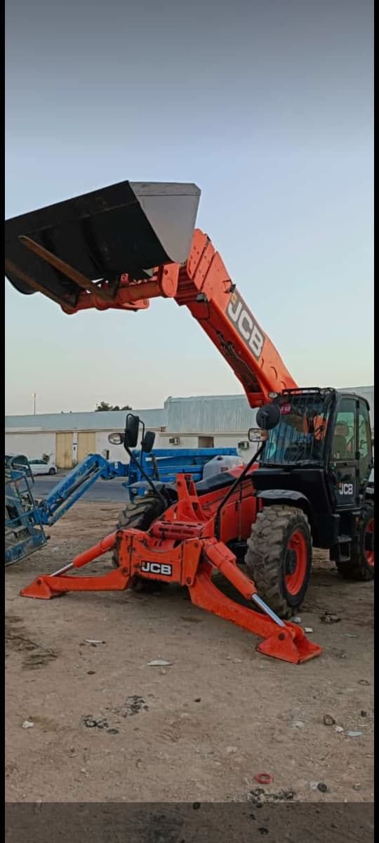 Telehandler with bucket attachment loading material at dusk